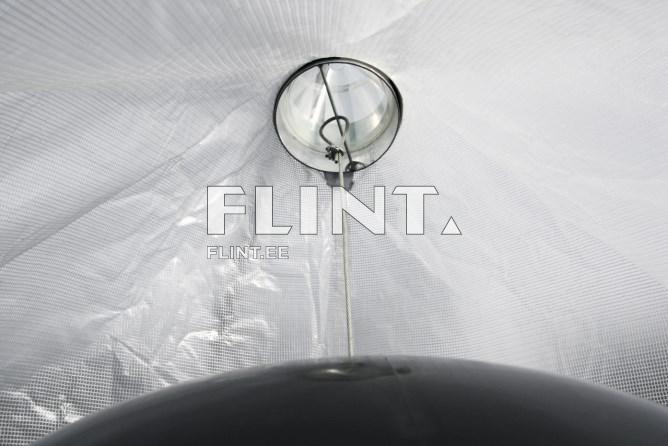 Kujutis näitab musta kuppli või mütsi alamist osa, mille peal on selge valgusti, mis on kinnitatud naelu kaudu. Taust on heledat värvi ja tekstuuriga, mis näeb välja nagu võrkpind.