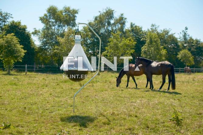 Pildil on heinasaagidega varustatud seade, mis on kinnitatud roostevabast terasest raami külge. Seade asub avaras rohelises väljas, kus murul on kaks musta hobust, kes söövad. Taustal on rohelised puud ja sinine taevas.