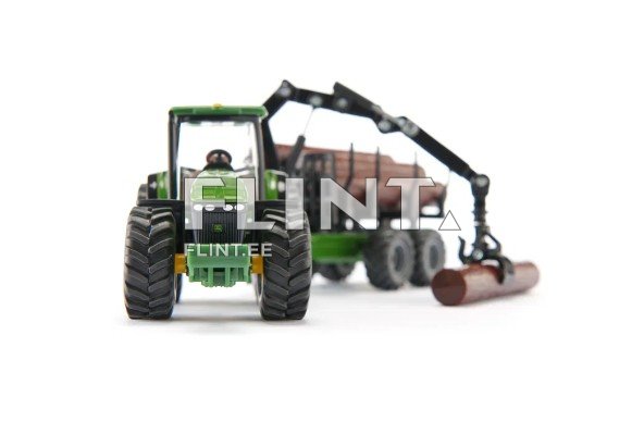 Pildil on roheline traktor, millel on mustad rehvid. Traktoril on taga puude vedamiseks mõeldud haagis, mis kannab puid. Traktori ees on nähtav kabiin ja juhikoht.