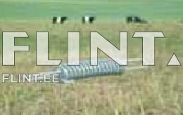 Pildil on heina- või viljacuttimine, millel on metallist keerdkujulised osad. Taustal on rohelised põllud ja mõned mustad valged karjad.