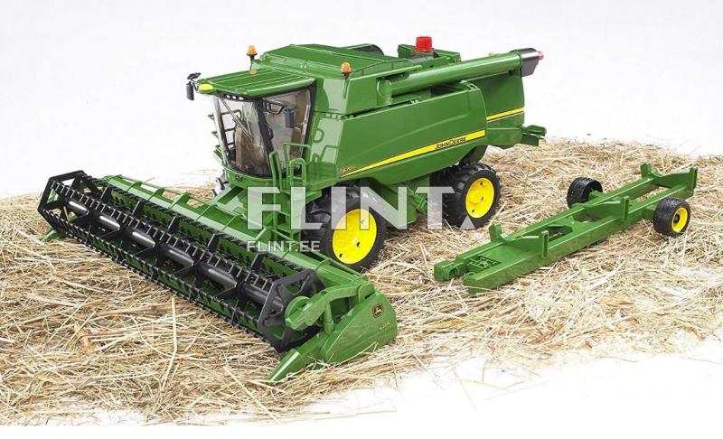 Pildil on roheline kombain, millel on must peadekood ja kollased rattad, asetatud heina peale. Kombainil on suured aknad ja punane lamp katuse peal. Selle kõrval on roheline tarvik, millel on mustad rattad.