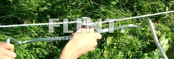 Käsi hoiab metallist tööriista, mis on ühendatud nööriga. Roheline murupind on taustal.