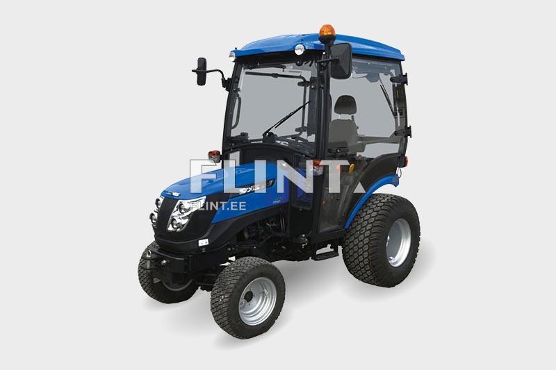 Sinine traktor, millel on suletud kabiin, suurde jaoturisse on paigaldatud vilkur. Kabiinis on nähtav iste ja rool.