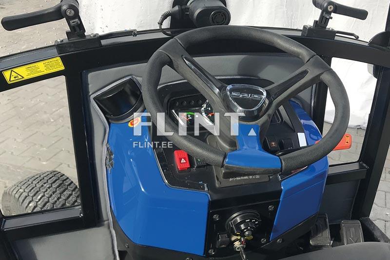 Tootepildil on traktor, mille juhtimisseade asub keskosas. Rool on musta värvi ja selle keskel on hõbedane detail. Seadme paremal pool on punane ja sinine nupp.