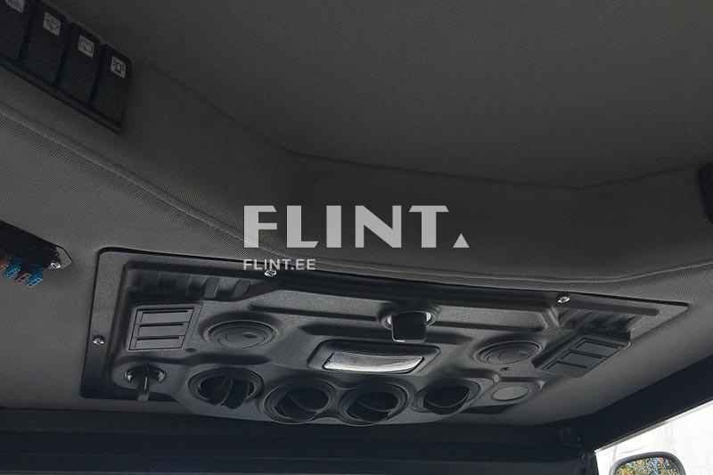 Pildil on sõiduki sisekatuse ülemine osa. Üks külg sisaldab lüliteid, mis on järjestatud neljaks ja on mustad. Keskel on must paneel, mis sisaldab erinevaid nuppusid ja avasid. Nupud on erineva kujuga ja suurusega, mille seas on ka helisüsteemile kuuluvad avad.