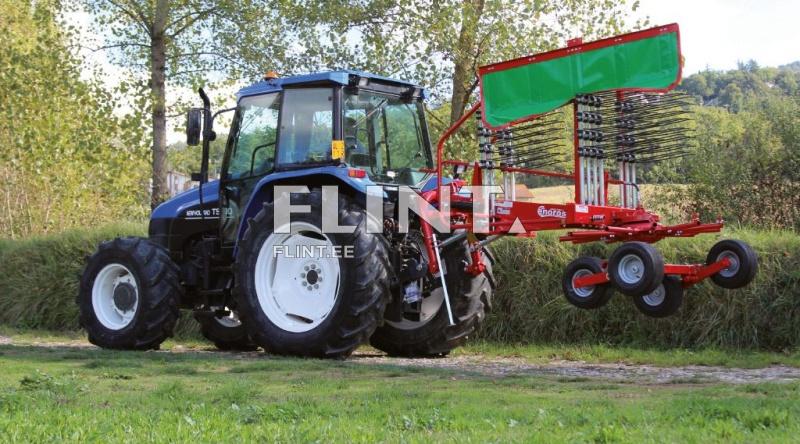 Sinise traktoriga, millel on punane niiduk, sõites rohelises väljakus, taustal puud.