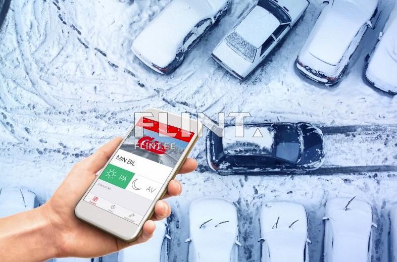 Pildil on nutitelefon, mille ekraanil on rakendus, kus on näha autot ja hoolduse valikud. Taustal on auto parkimisala, kaetud lume ja jääga, kus on mitu pargitud autot.