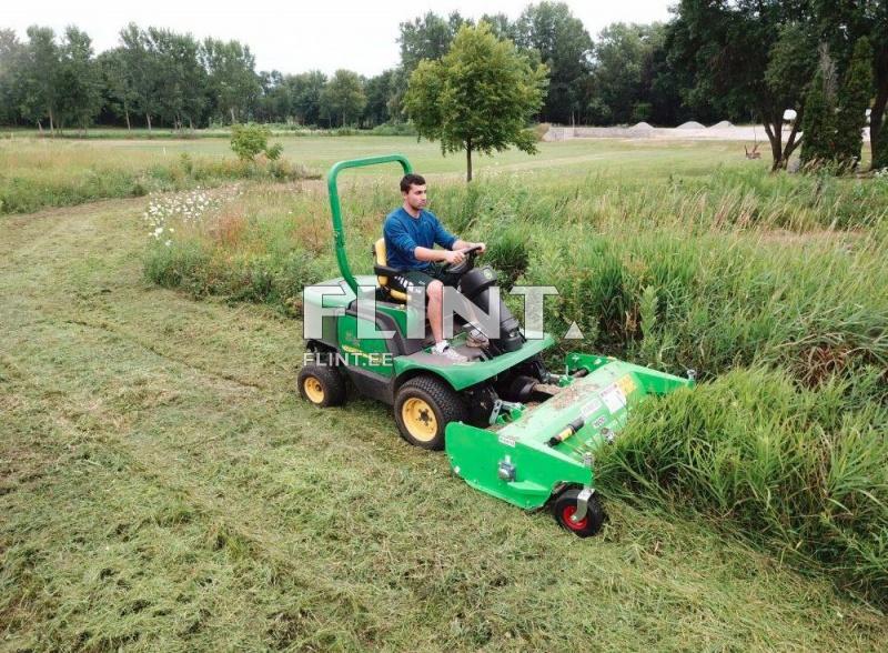 A man is operating a green riding mower equipped with a mower deck, cutting grass in a field surrounded by trees.