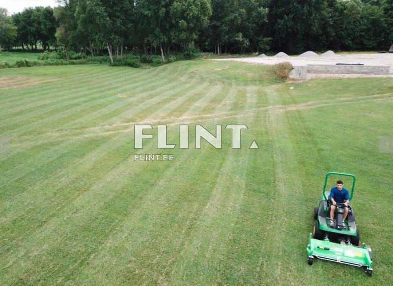 Roheline muruniiduk, millel sõidab noormees, ajab sirgeid riba, taustal rohelised puud ja avatud muruplats.